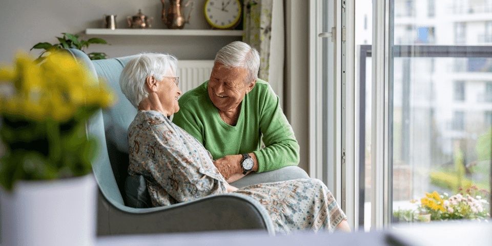 Older couple talking together at home beside a bright window
